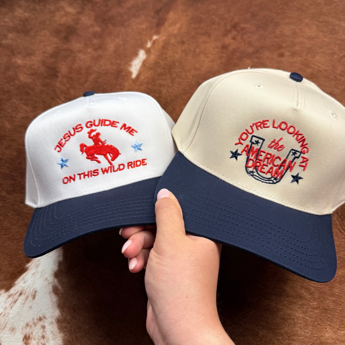 Embroidered western themed trucker hat in navy and beige says "you're looking at the American dream" with a horseshoe and stars and jesus guide me on this wild ride trucker hat is featured with it.