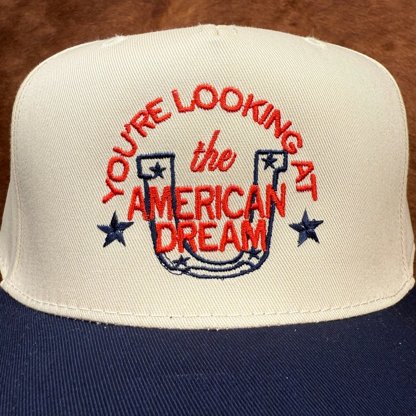 Embroidered western themed trucker hat in navy and beige says "you're looking at the American dream" with a horseshoe and stars