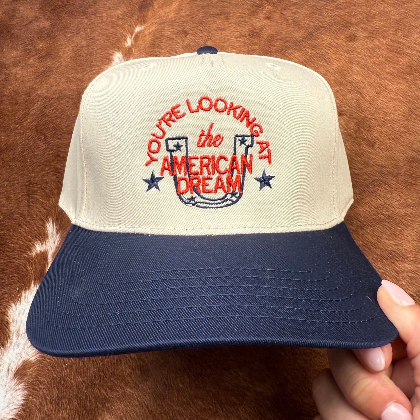 Embroidered western themed trucker hat in navy and beige says "you're looking at the American dream" with a horseshoe and stars