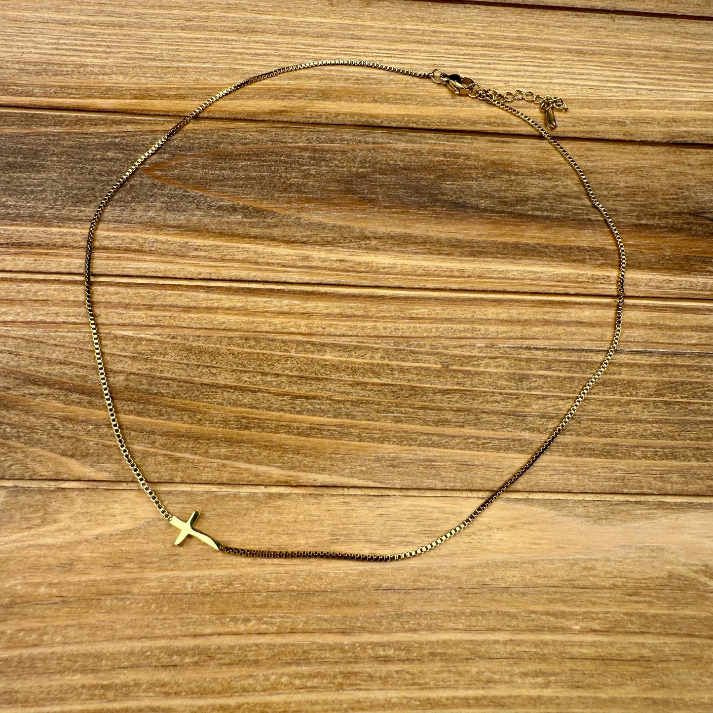 Gold necklace with a small cross pendant on a wooden surface