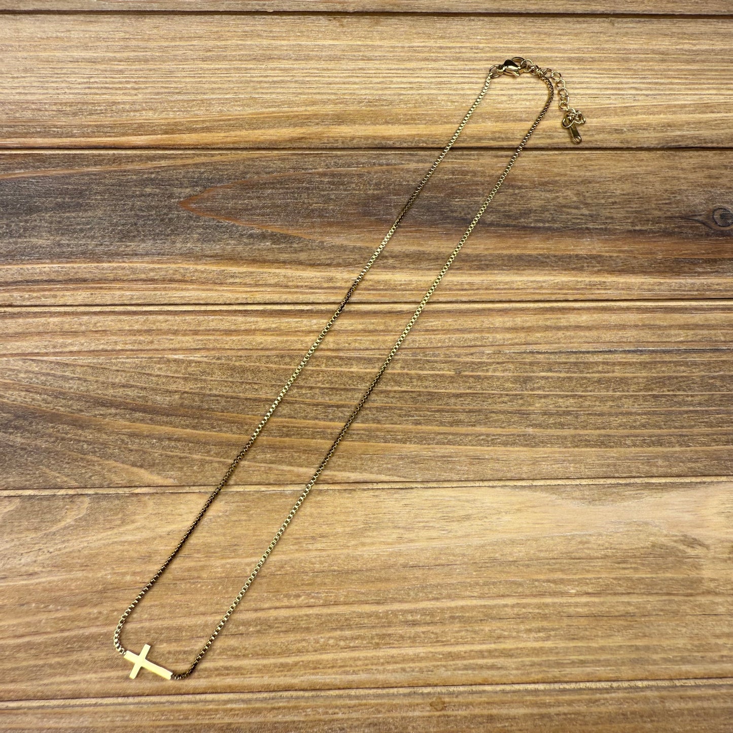 Gold necklace with a small cross pendant on a wooden surface