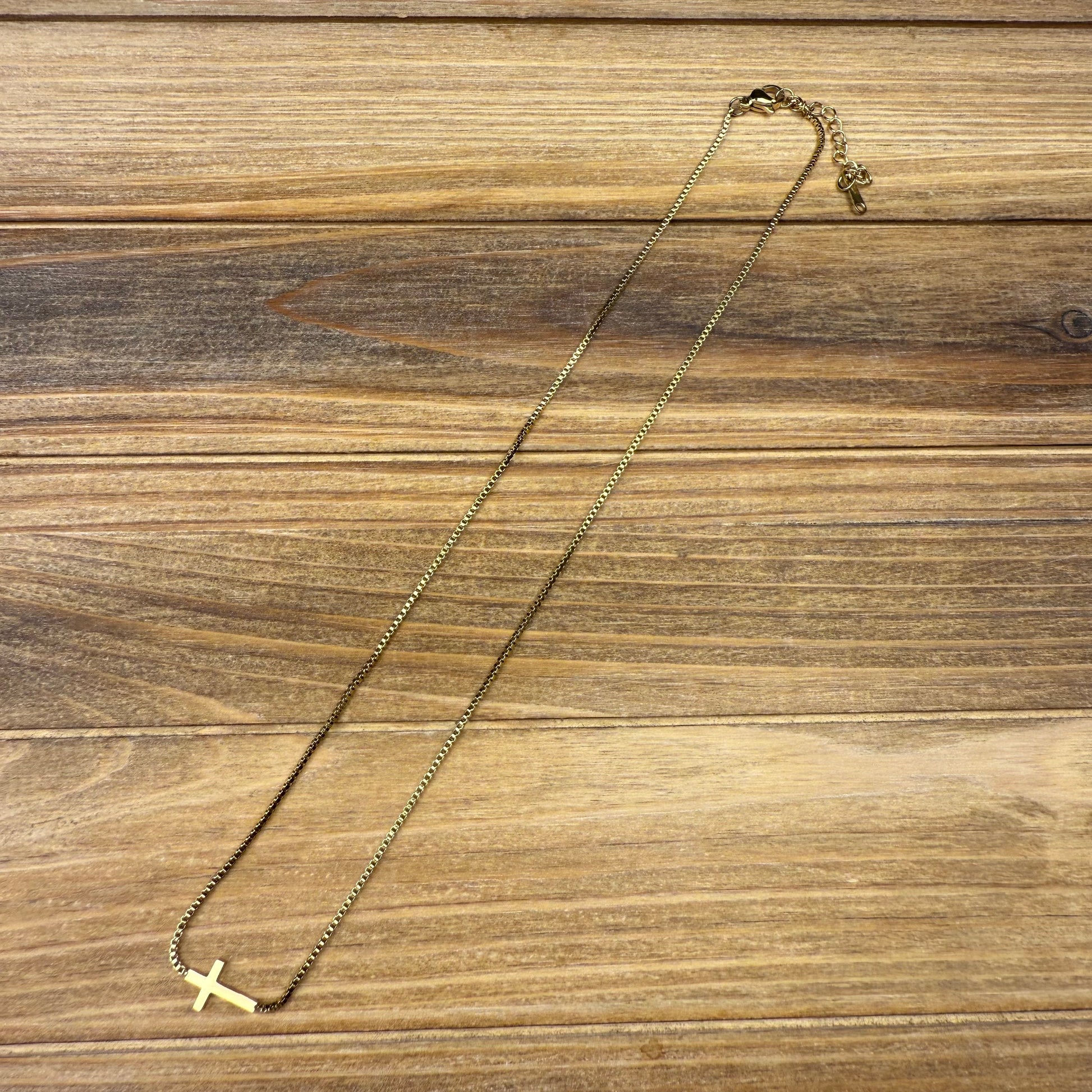 Gold necklace with a small cross pendant on a wooden surface