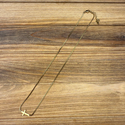 Gold necklace with a small cross pendant on a wooden surface