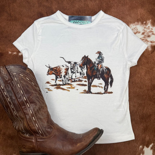 White baby tee with cowboy graphic and cattle western styled top for country concerts or rodeos.